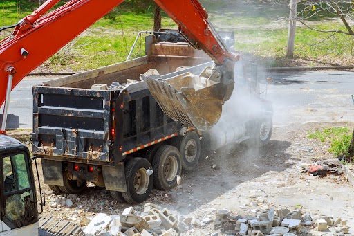 Excavator scoop truck loading construction waste into a dump truck